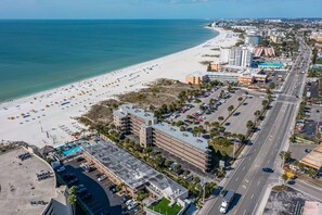 An aerial view of a coastal city with a beach, parking lots, and buildings.