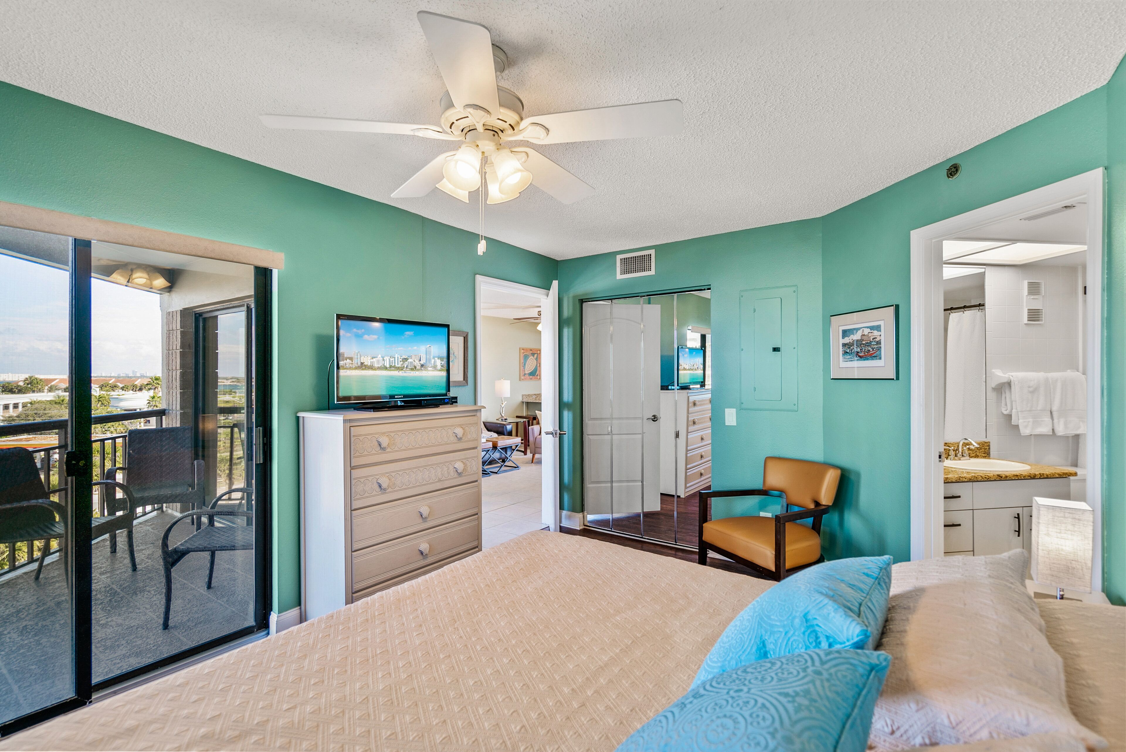 A bedroom with a bed, a TV, a chair, a dresser, and a balcony with chairs.