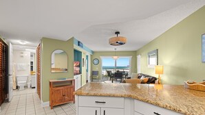 A kitchen with a granite countertop, wooden cabinets, and a view to the outside. - 🌅 Prime View Condo — Gulf Strand Resort, St. Pete Beach (St Pete Beach)
