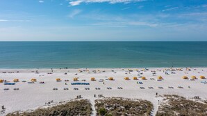 A beach with numerous sunbeds and umbrellas, a clear sky, and the ocean in the background. - 🌅 Prime View Condo — Gulf Strand Resort, St. Pete Beach (St Pete Beach)