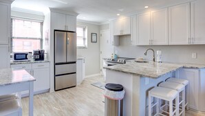 A modern kitchen with white cabinets, stainless steel appliances, a marble countertop, and a built-in oven.