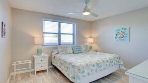 A bedroom with a bed, bedside lamps, a window, a ceiling fan, and a wall art piece.