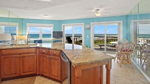 A kitchen with a large island, wooden cabinets, and a view of the ocean through large windows.