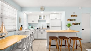 Una cocina moderna con armarios blancos, una isla de madera con taburetes y una decoración náutica con un velero.