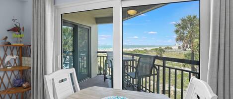 A balcony with a view of the beach, a table with chairs, and a decorative shelf with items.