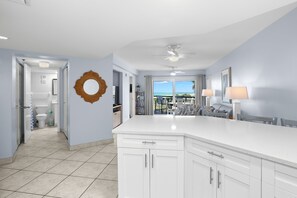 A modern kitchen with a large island, white cabinetry, and a view to the outside.