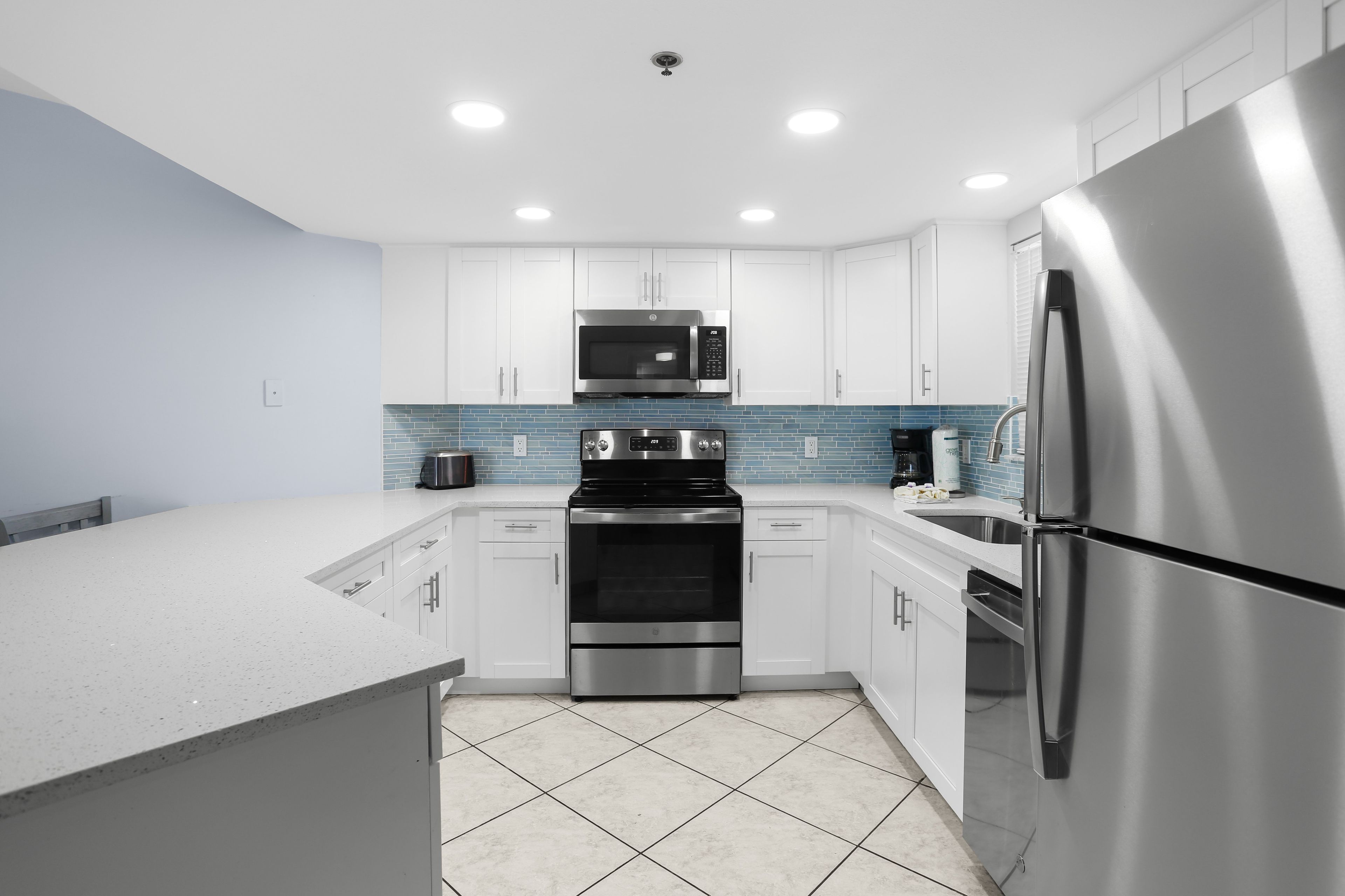 A modern kitchen with white cabinets, stainless steel appliances, and a blue-tiled backsplash.