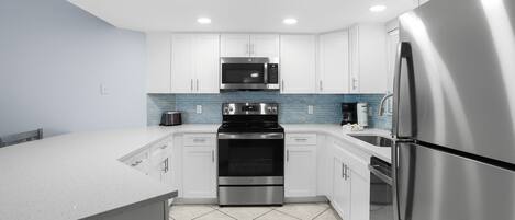 A modern kitchen with white cabinets, stainless steel appliances, and a blue-tiled backsplash.
