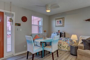 A dining area with a table and chairs, a ceiling fan, a clock, and a window with blinds.