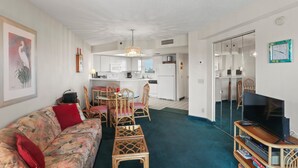 Ein Wohnzimmer mit einer Couch, Sesseln, einem Fernseher und einem Essbereich mit Tisch und Stühlen.