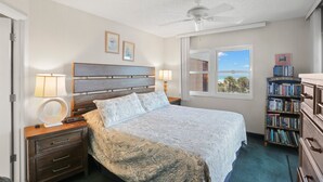 Ein Schlafzimmer mit Bett, Nachttischlampen, Deckenventilator, Fenster mit Blick und Bücherregal.