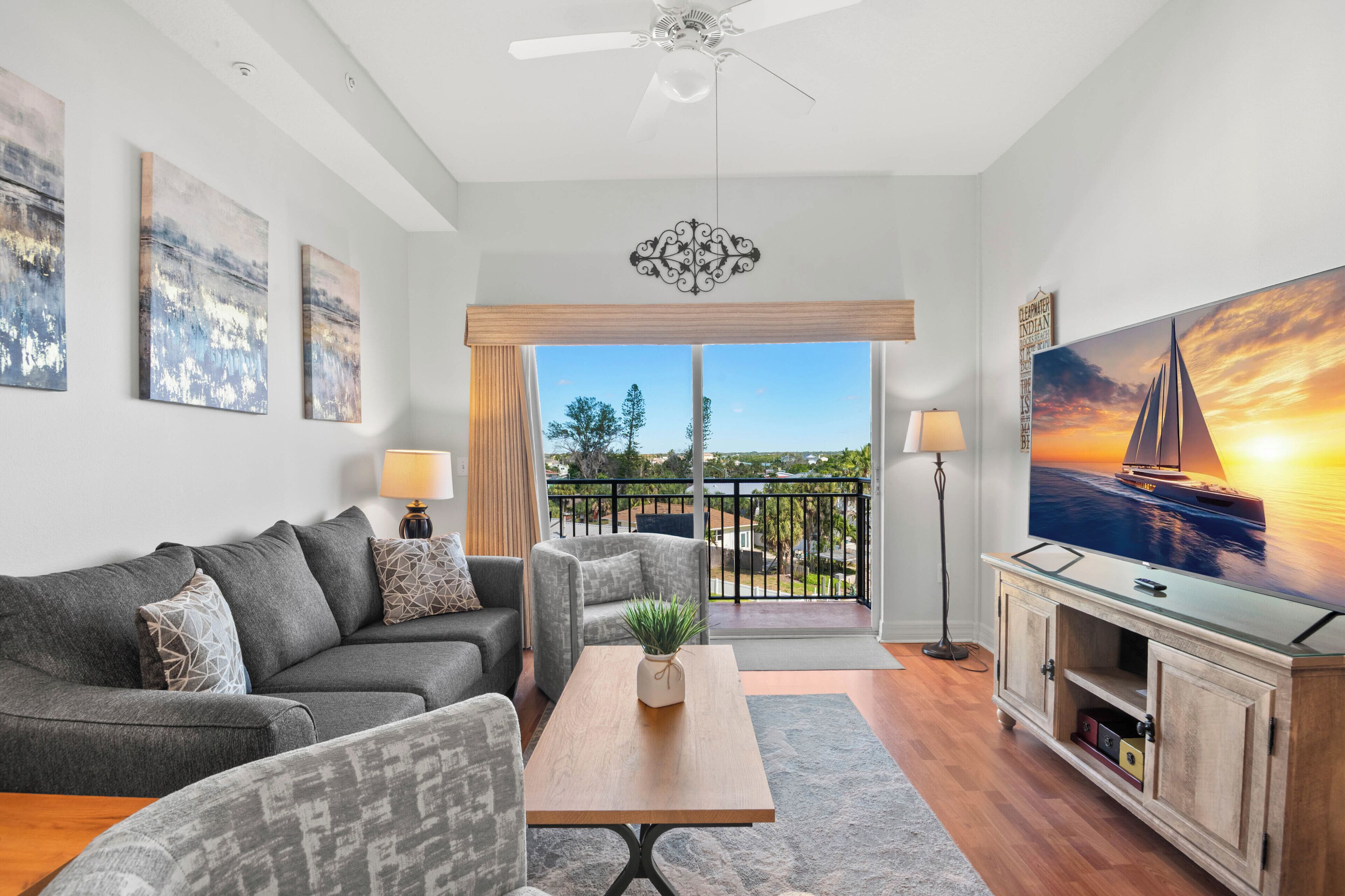 A modern living room with a sofa, armchairs, a coffee table, a TV, and a balcony with a view.