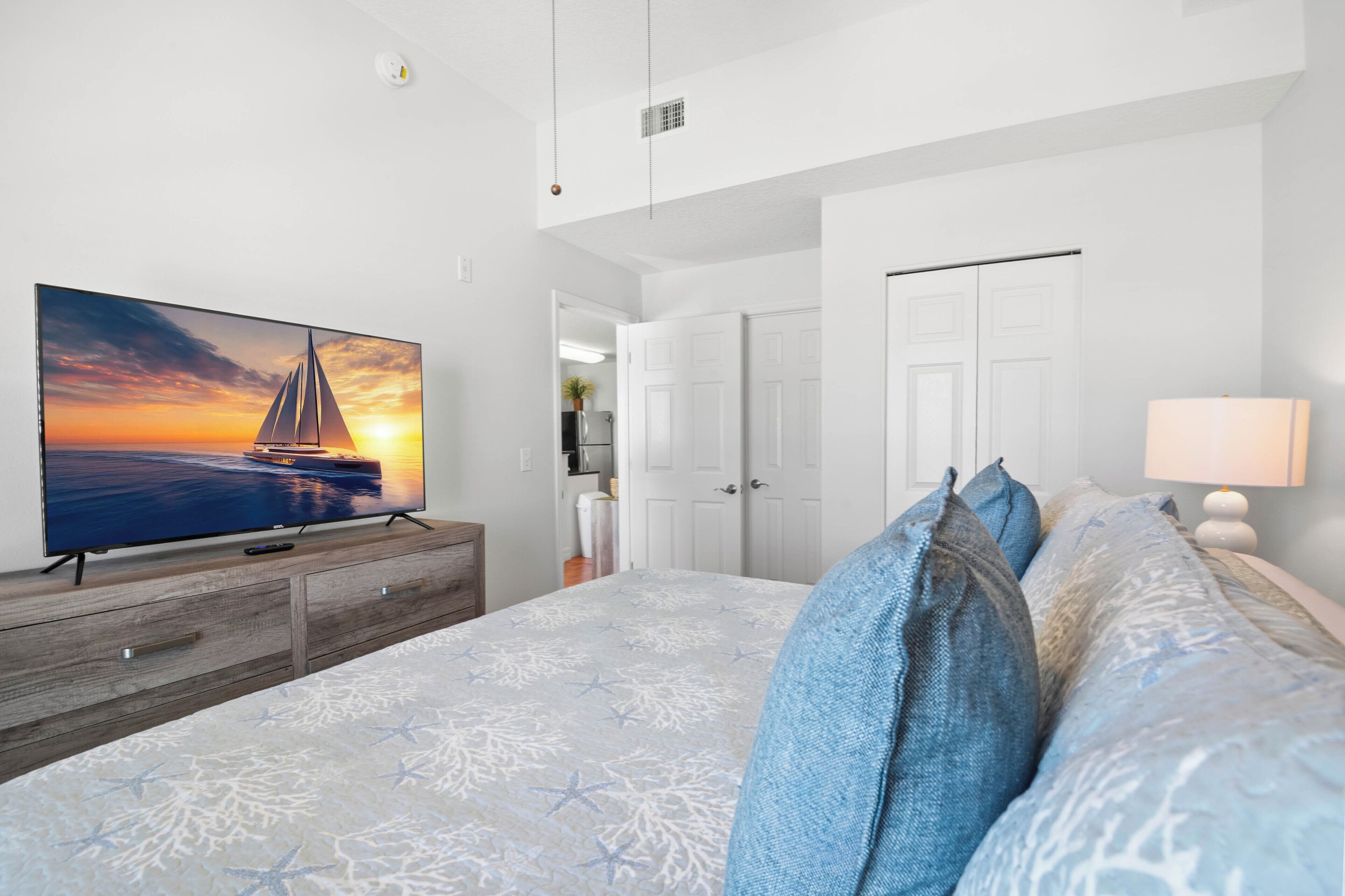 Une chambre avec un grand lit, un téléviseur posé sur une commode en bois et une porte donnant sur une salle de bain.