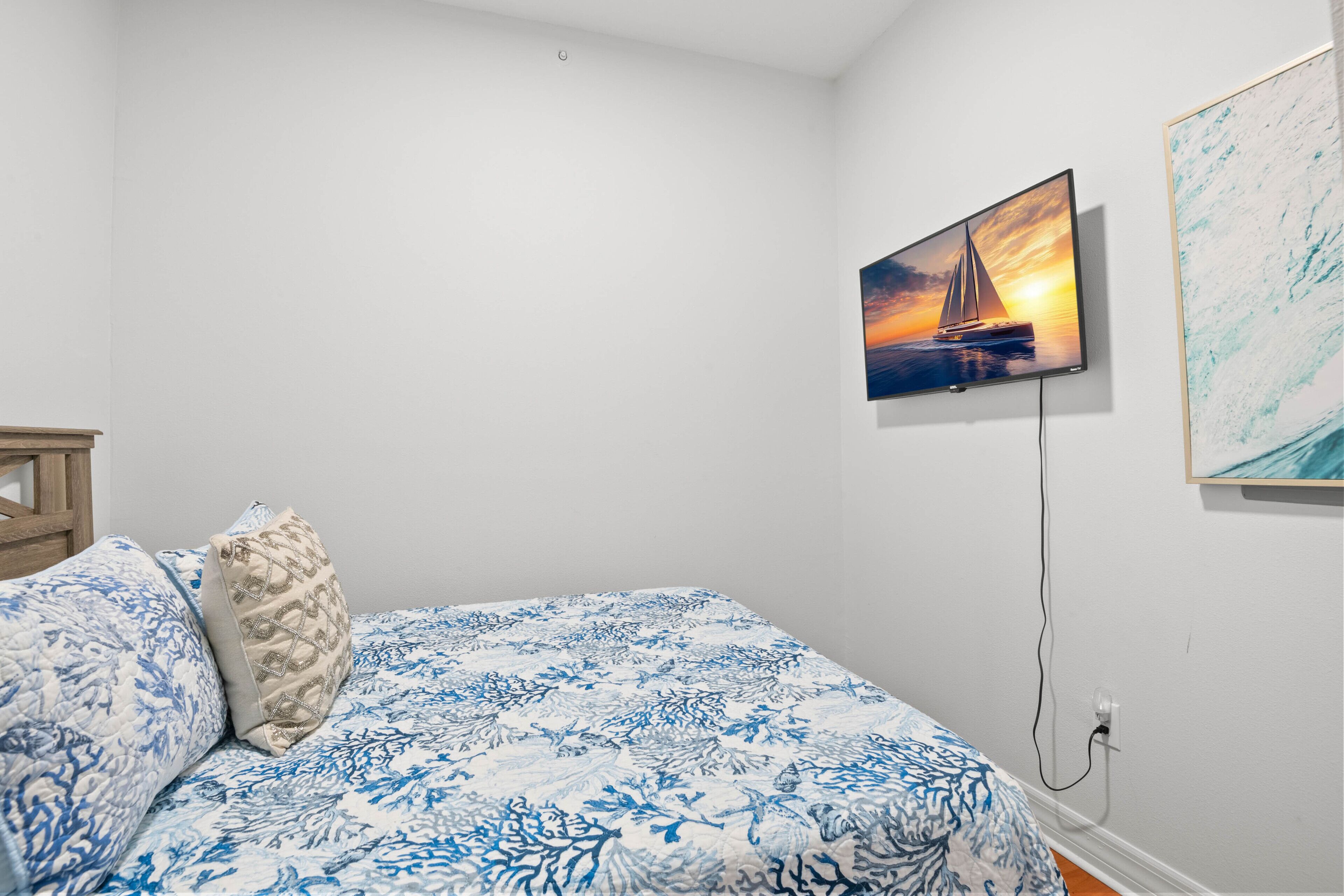 Un dormitorio con cama, televisor montado en la pared y un cuadro.