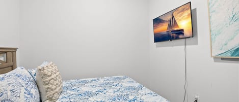 Un dormitorio con cama, televisor montado en la pared y un cuadro.
