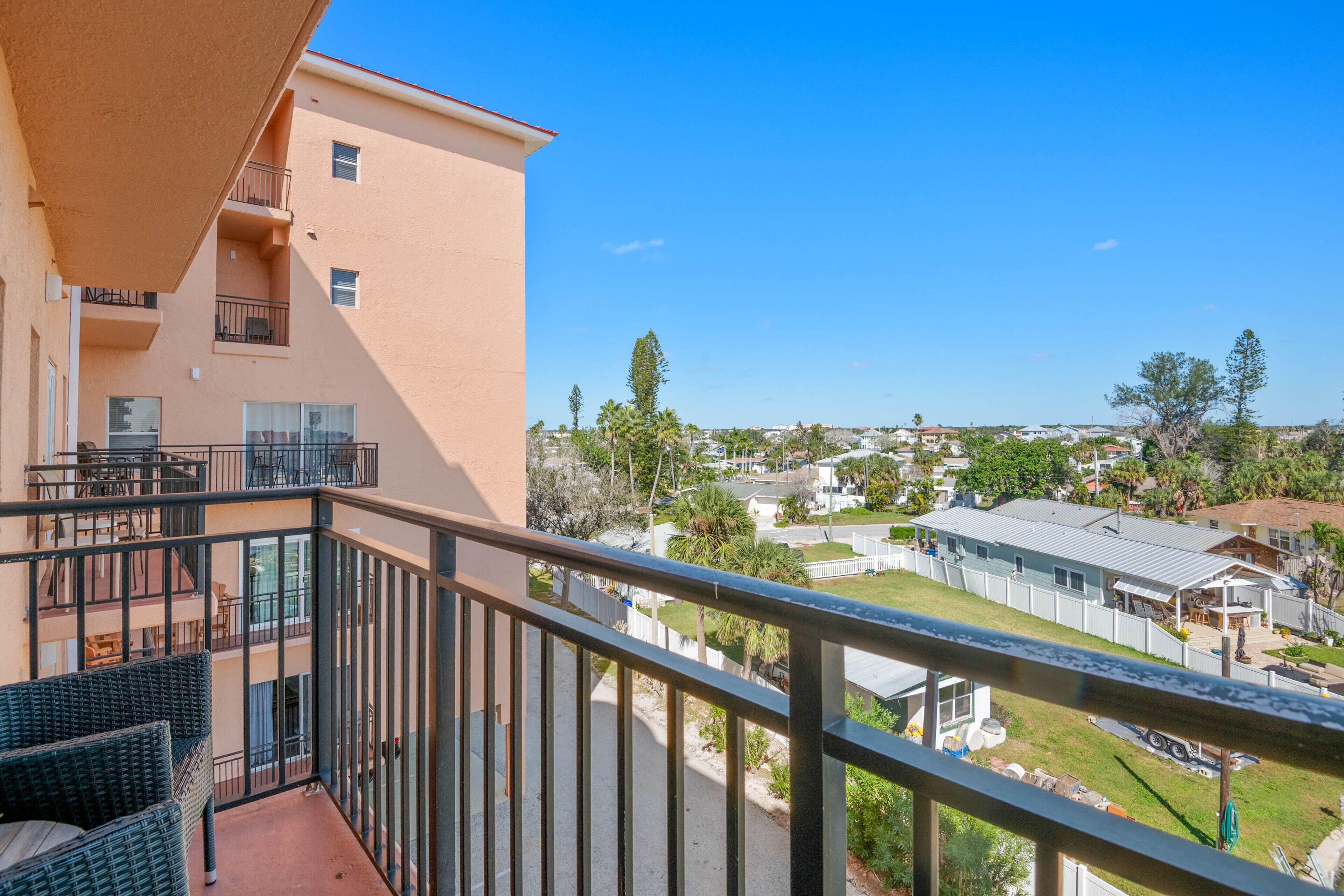 A balcony with wicker furniture, a view of a residential area, and a clear blue sky.