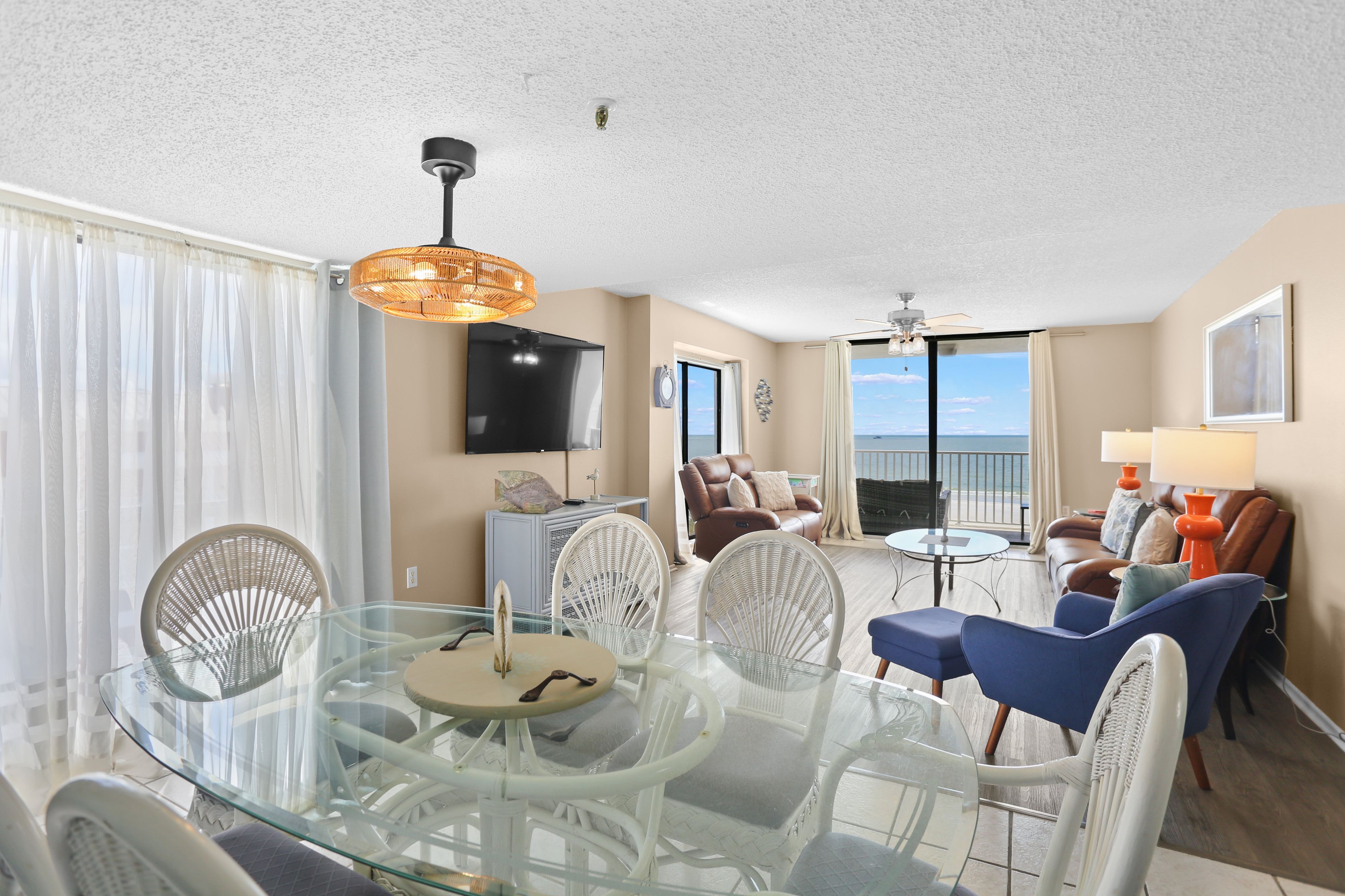 A spacious living area with a glass dining table, comfortable seating, a television, and a view of the ocean.