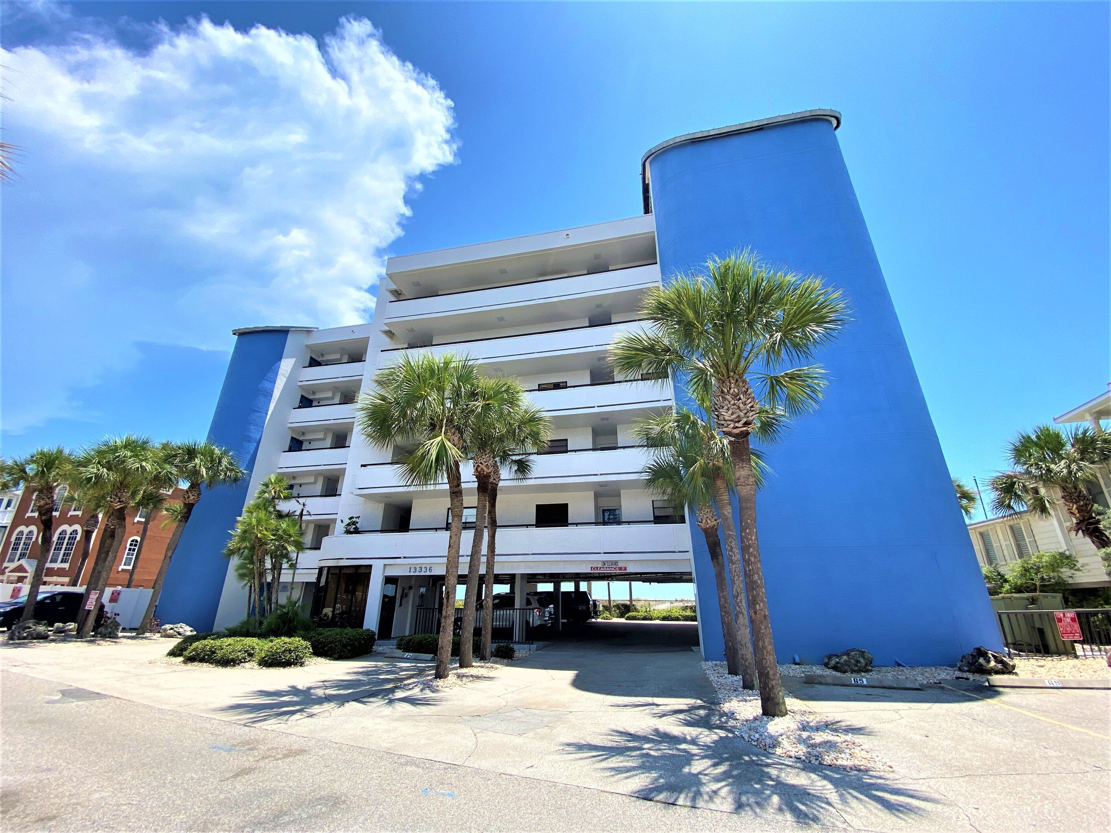 A multi-story hotel with a blue facade, palm trees in front, and a clear sky.
