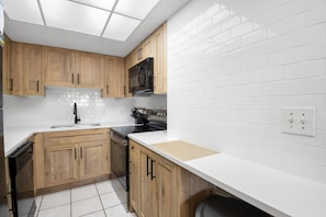 A modern kitchen with wooden cabinets, a black microwave, and white countertops.