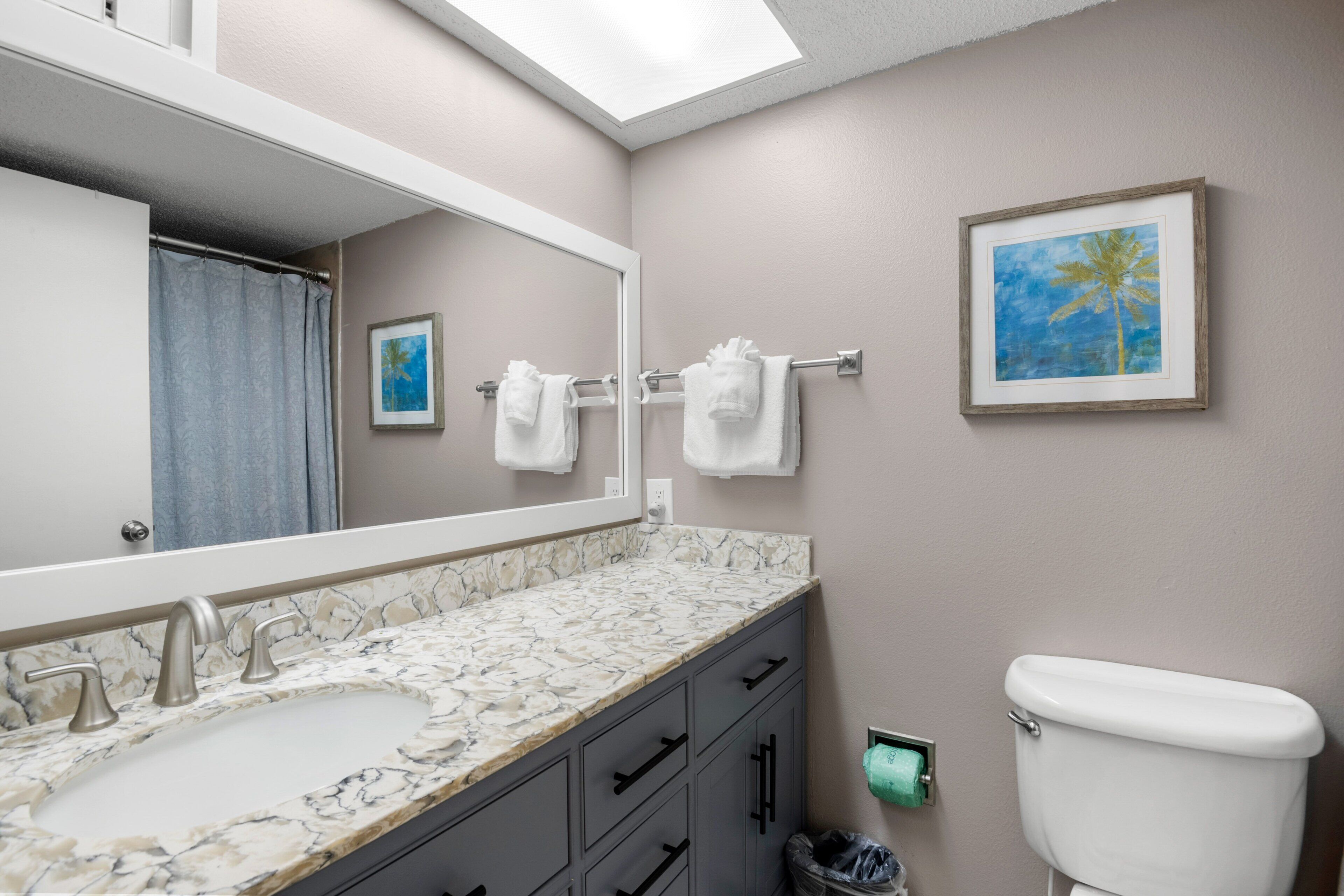 A bathroom with a marble sink, a toilet, a towel rack with towels, a framed picture on the wall, and a trash can.