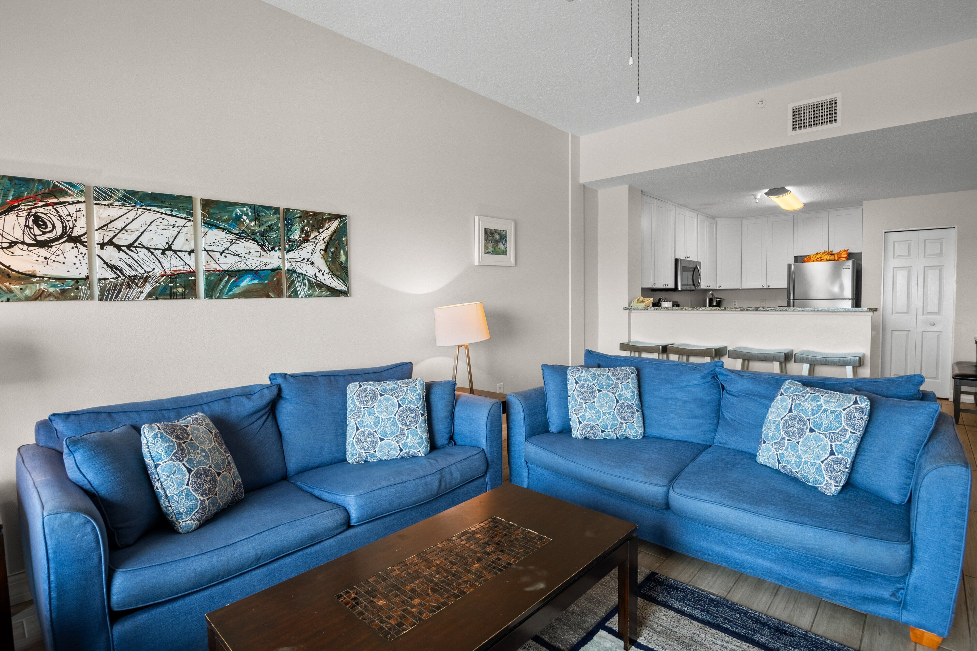 A modern living room with two blue sofas, a coffee table, and artwork on the wall.