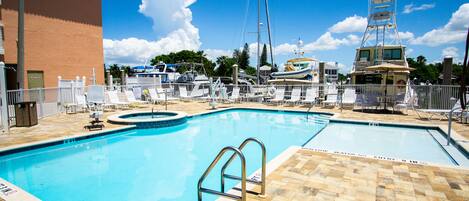 A swimming pool with a diving board, lounge chairs, and a boat docked nearby.