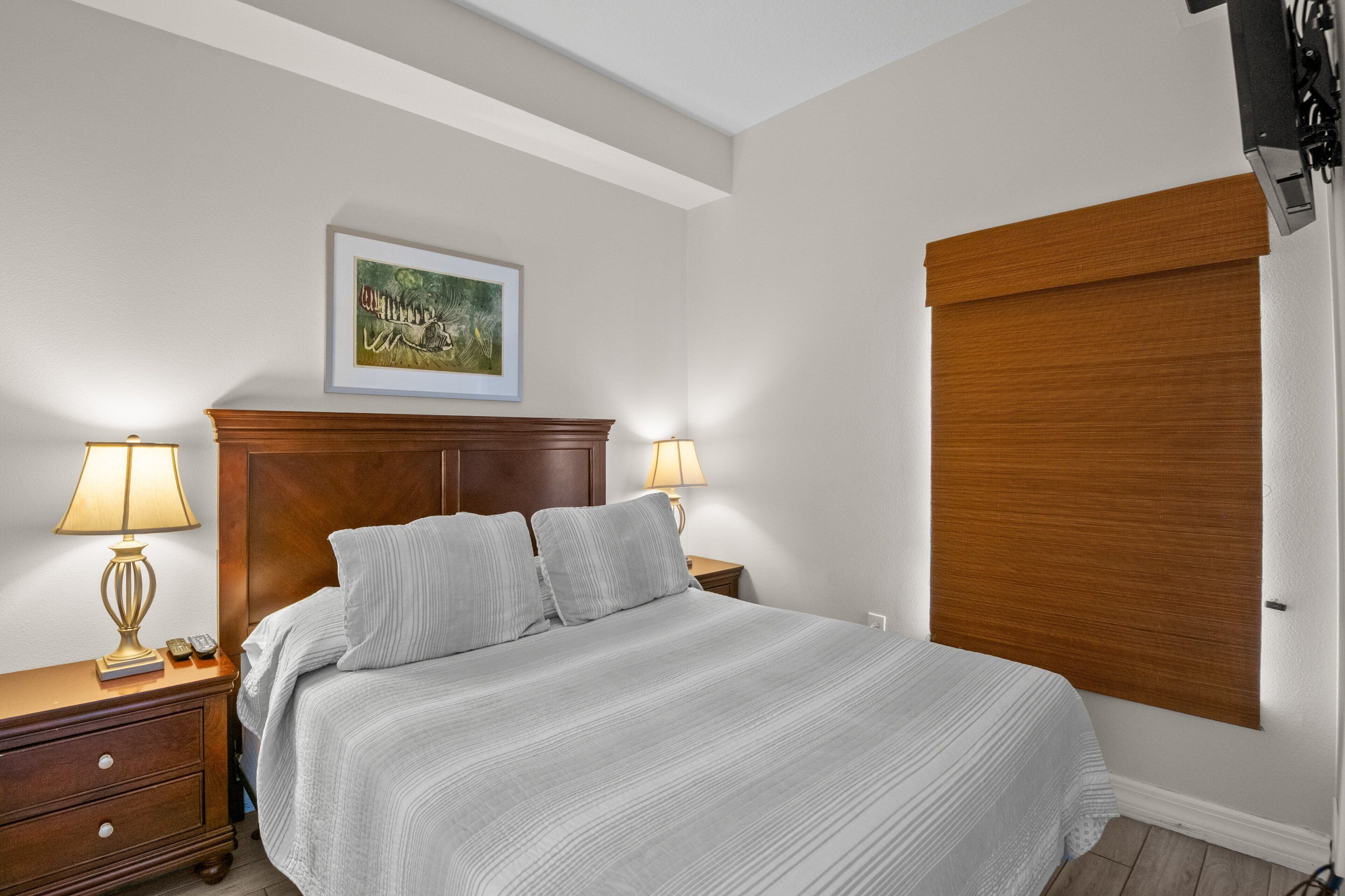 Un letto rifatto con una testiera, due lampade da comodino, un comodino con una lampada e un quadro incorniciato appeso al muro.