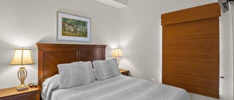 Un letto rifatto con una testiera, due lampade da comodino, un comodino con una lampada e un quadro incorniciato appeso al muro.