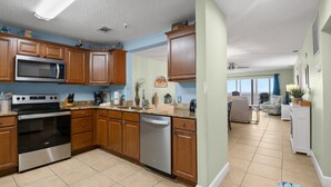 A modern kitchen with wooden cabinets, stainless steel appliances, and a view to the living area. - Sea Breeze 403 | Gulf-Front Balcony Views & Room to Unwind (Madeira Beach)
