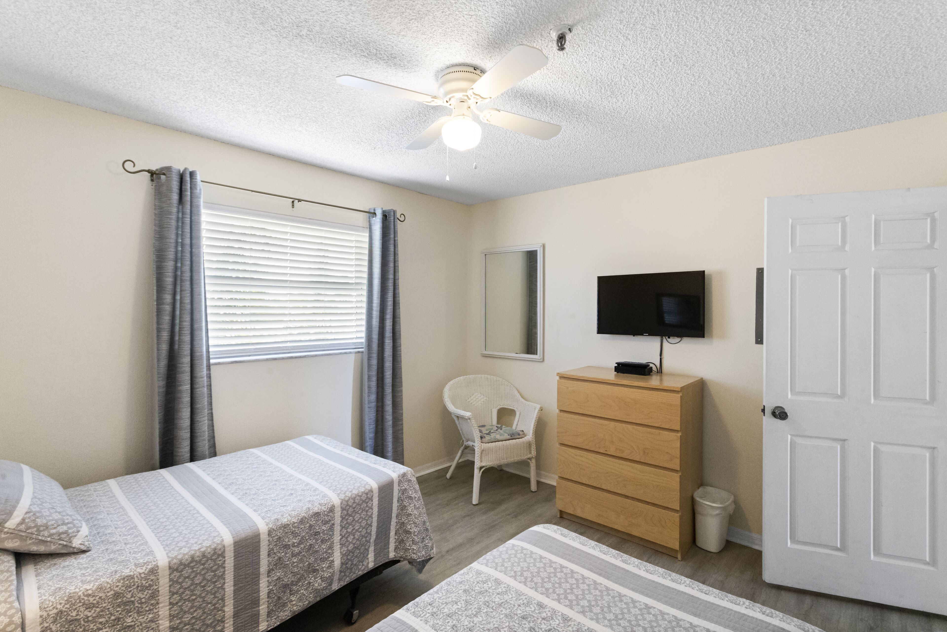 A bedroom with a bed, a dresser, a television, a ceiling fan, and a window with curtains.