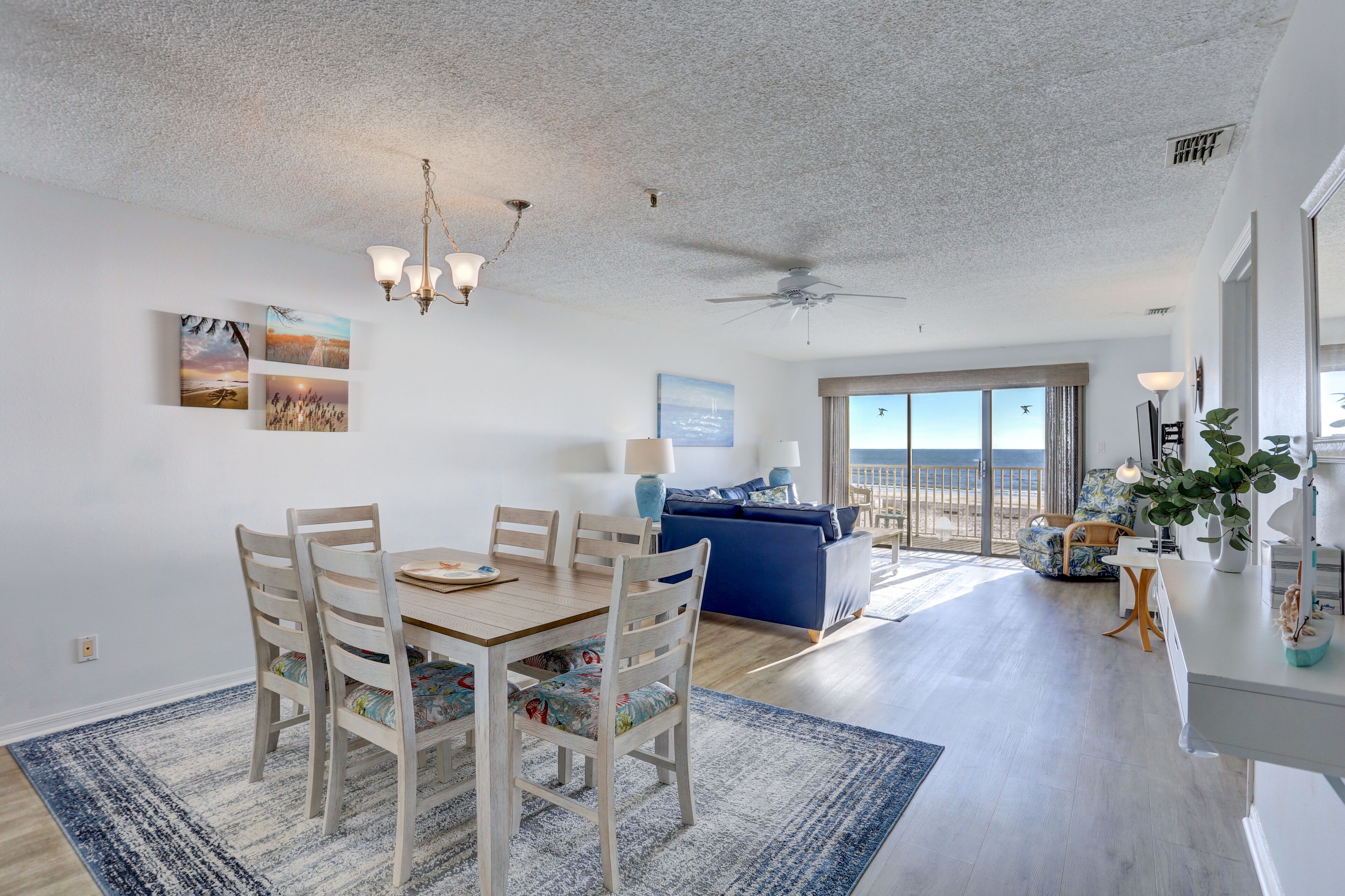 A spacious living area with a dining table, chairs, a blue sofa, and a view of the ocean through large windows.