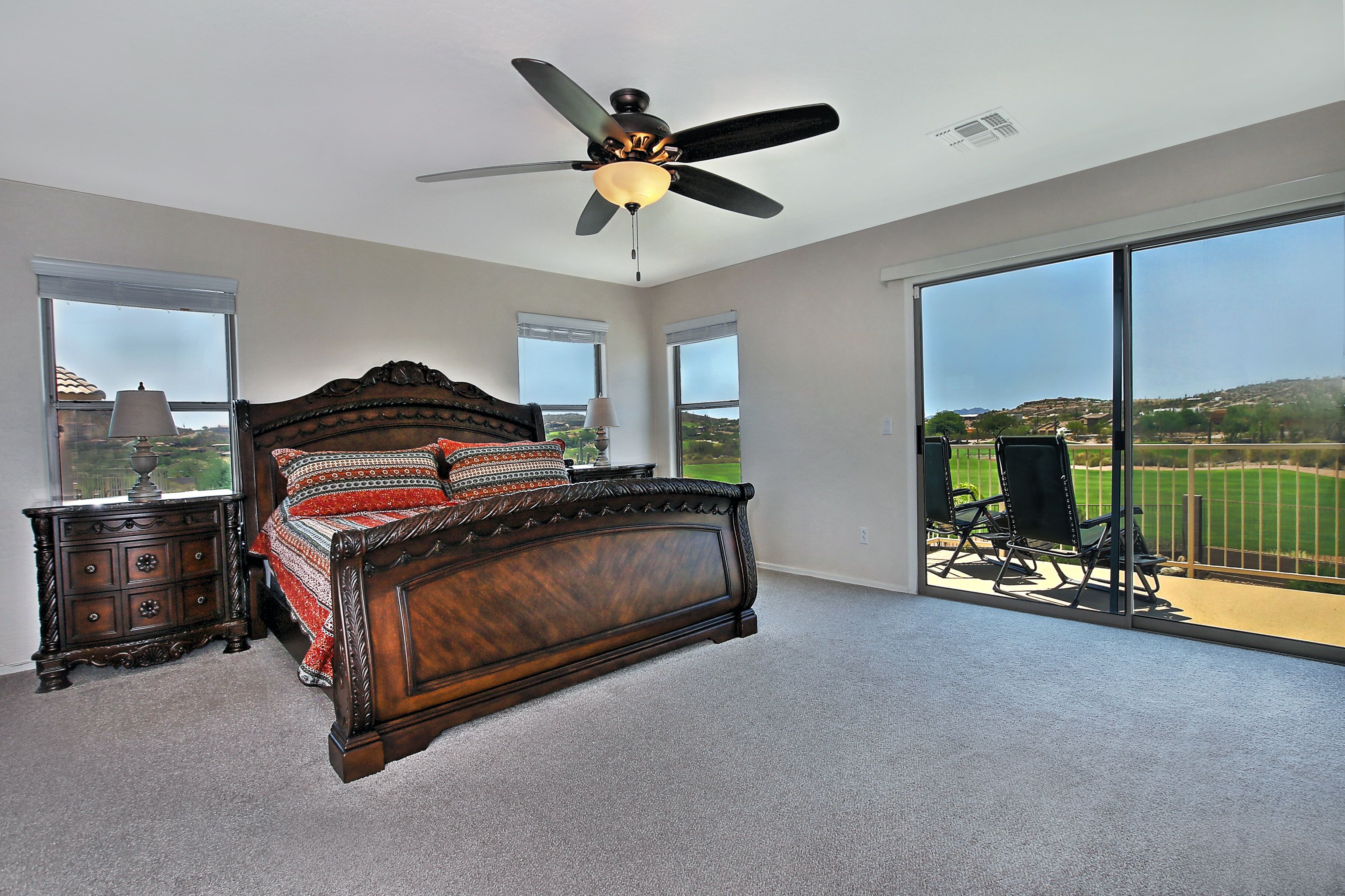 A bedroom with a large bed, a ceiling fan, and a view of a golf course through large windows.