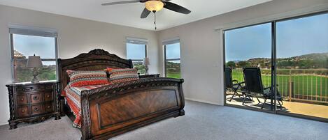A bedroom with a large bed, a ceiling fan, and a view of a golf course through large windows.