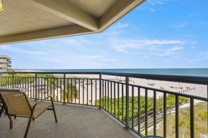 Ein Balkon mit Blick auf den Strand, ein Stuhl und ein Geländer.