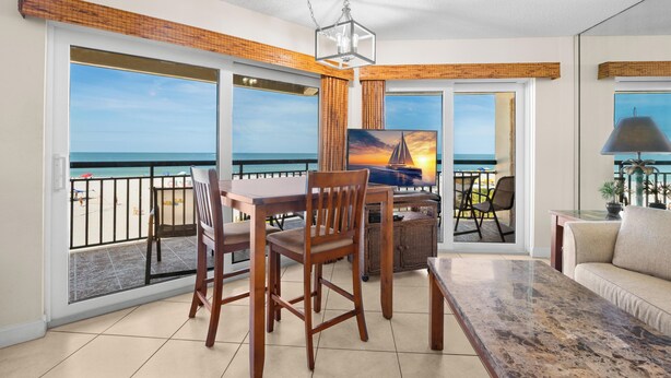 A balcony with a view of the sea, a dining table with chairs, a sofa, and a painting.
