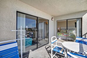 En balkon med bord og stole, en skydedør samt en seng med farverigt sengetøj.