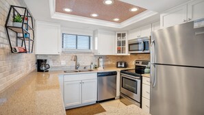 A modern kitchen with white cabinets, stainless steel appliances, a brick accent wall, and a built-in shelf with plants.