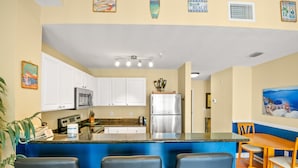 A kitchen with white cabinets, a stainless steel refrigerator, a blue countertop, and a wooden dining table with chairs.