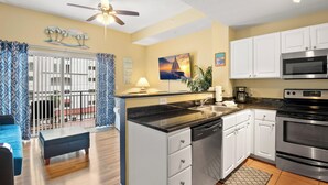 A modern kitchen with white cabinets, a black countertop, stainless steel appliances, and a ceiling fan.