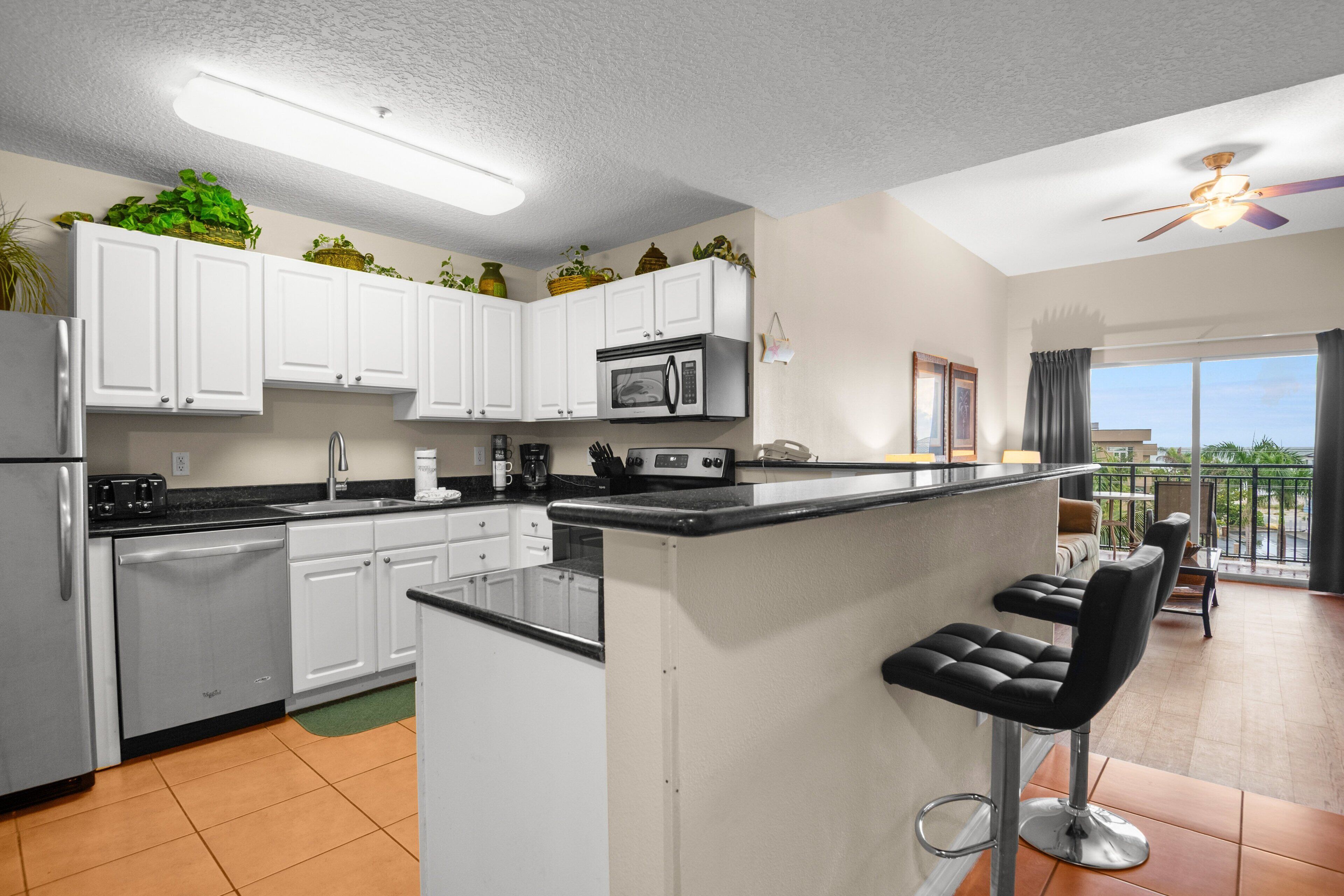 A modern kitchen with white cabinets, a stainless steel refrigerator, a microwave, and a bar area with black stools.