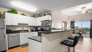 A modern kitchen with white cabinets, a stainless steel refrigerator, a microwave, and a bar area with black stools.