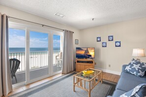 A living room with a large sliding glass door leading to a balcony overlooking the beach.