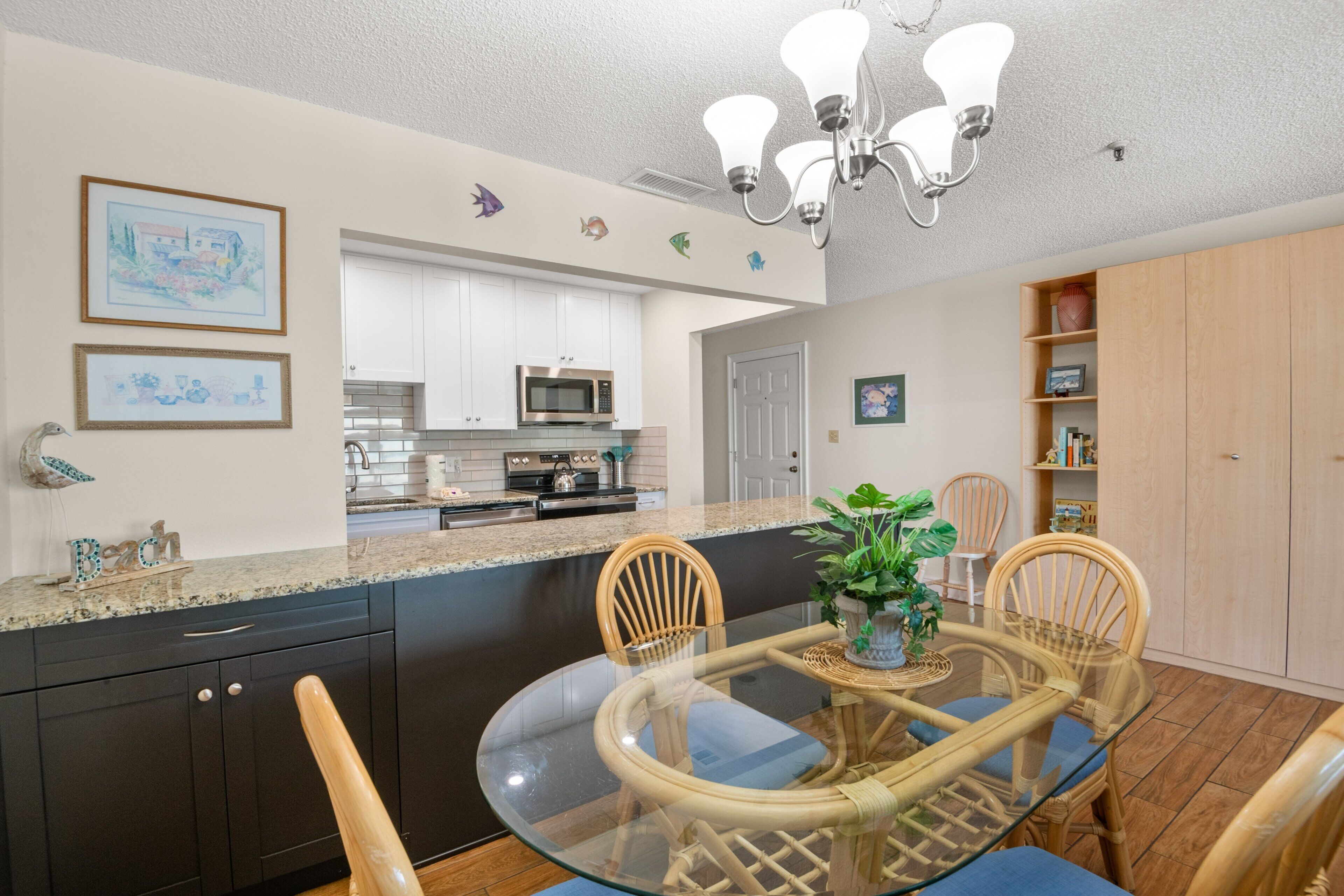 A modern kitchen with dark cabinets, a microwave, and a dining area with a glass table and wicker chairs.
