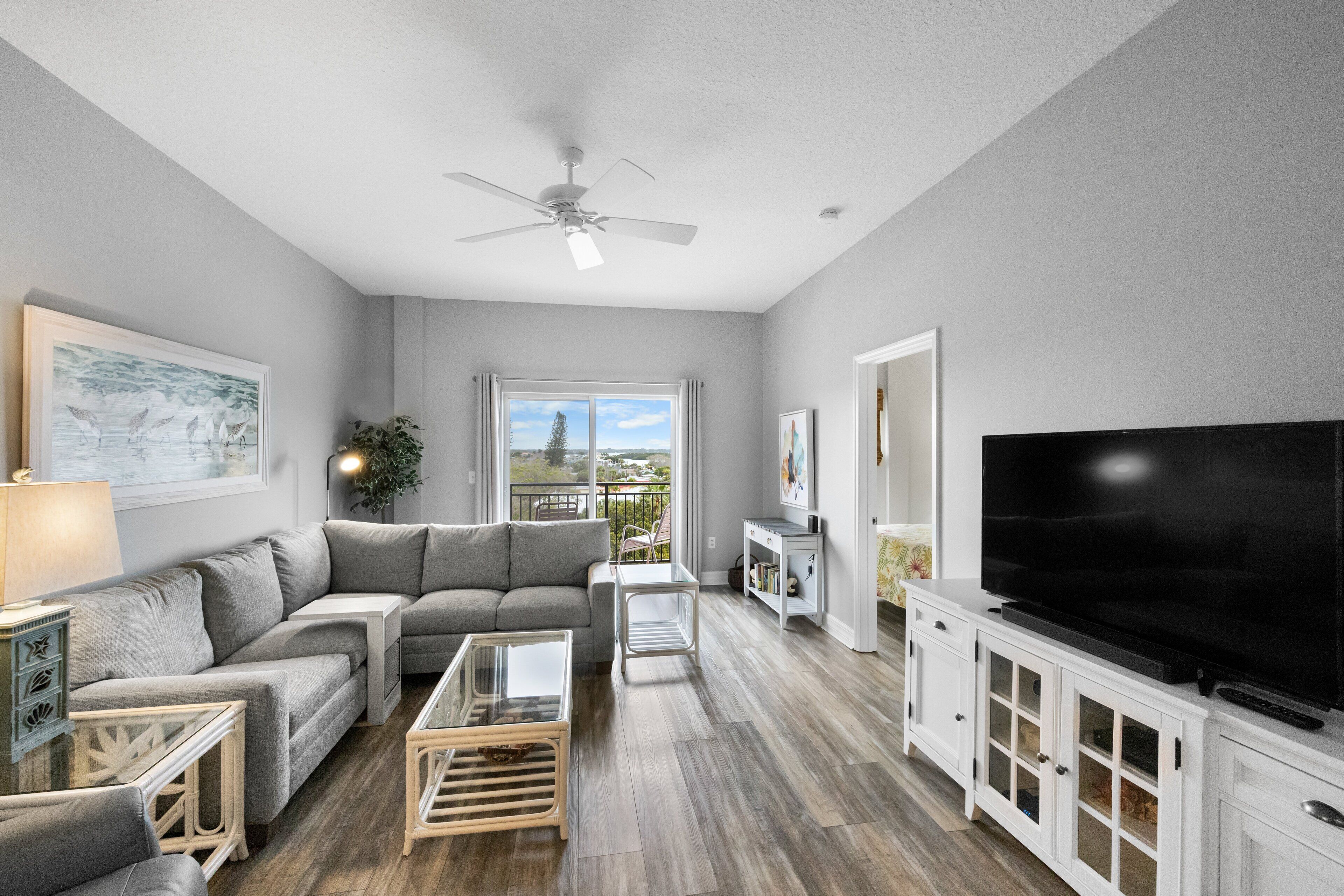 A modern living room with a grey sofa, a glass coffee table, and a flat-screen TV on a white cabinet.