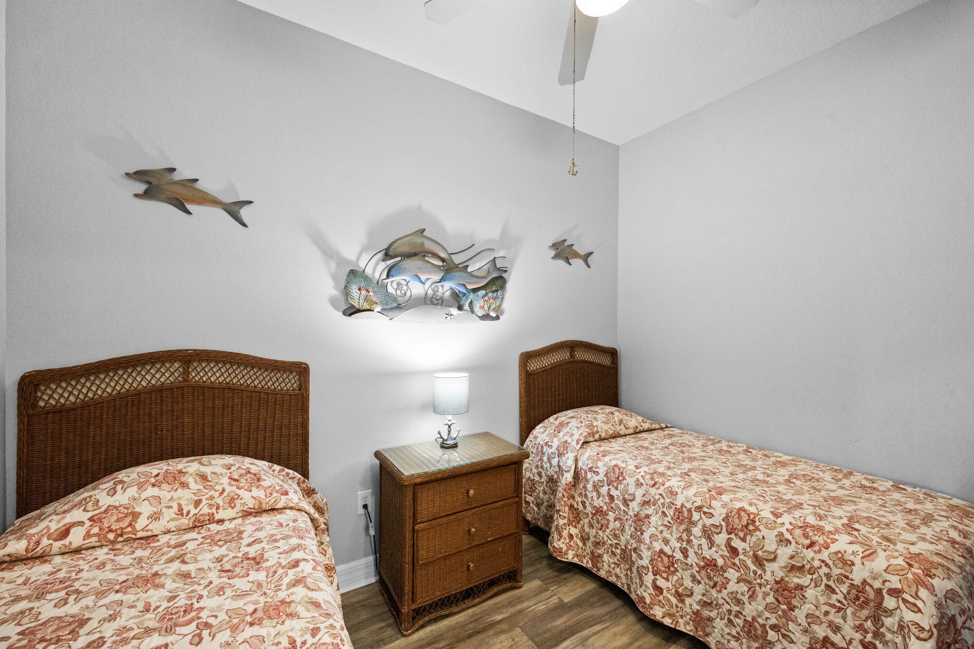 A bedroom with two single beds, a nightstand with a lamp, and wall art depicting fish.