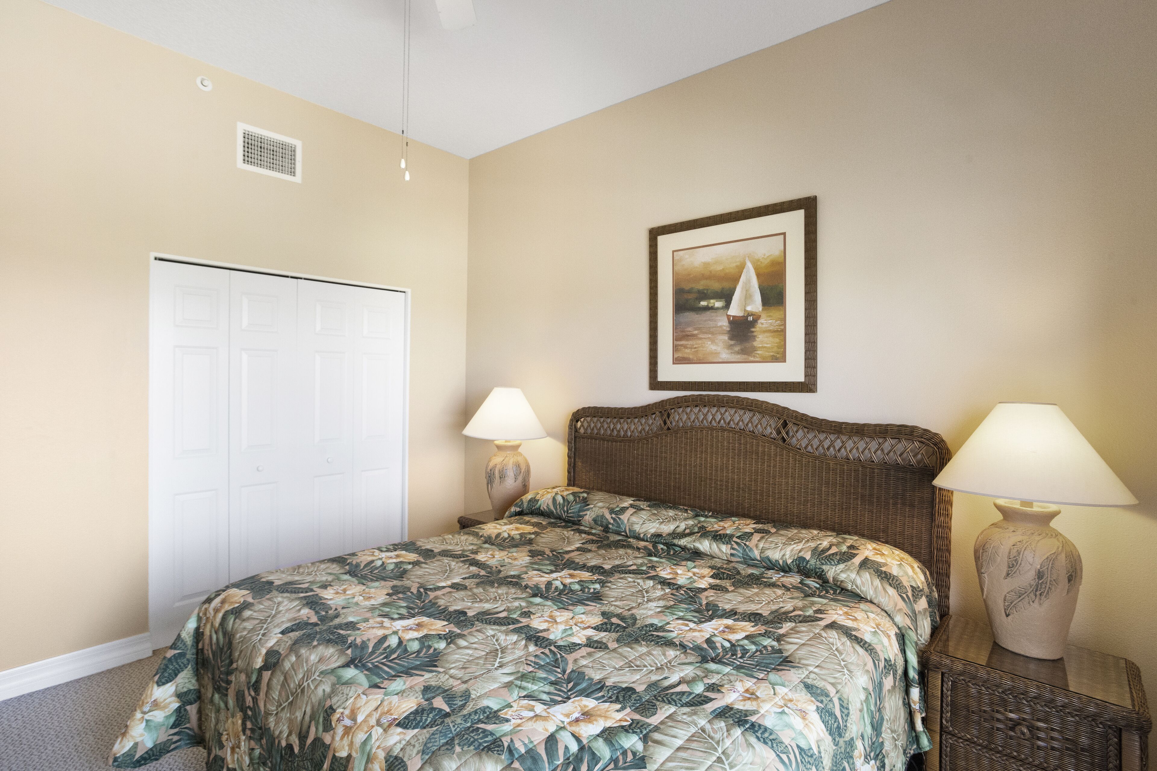 A bedroom with a bed, two bedside lamps, a framed picture on the wall, and a closet.