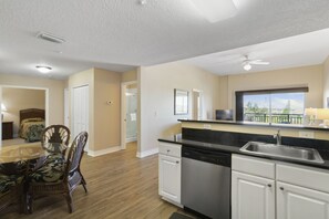 A modern kitchen with white cabinets, a dishwasher, and a large window offering a view of the outdoors.