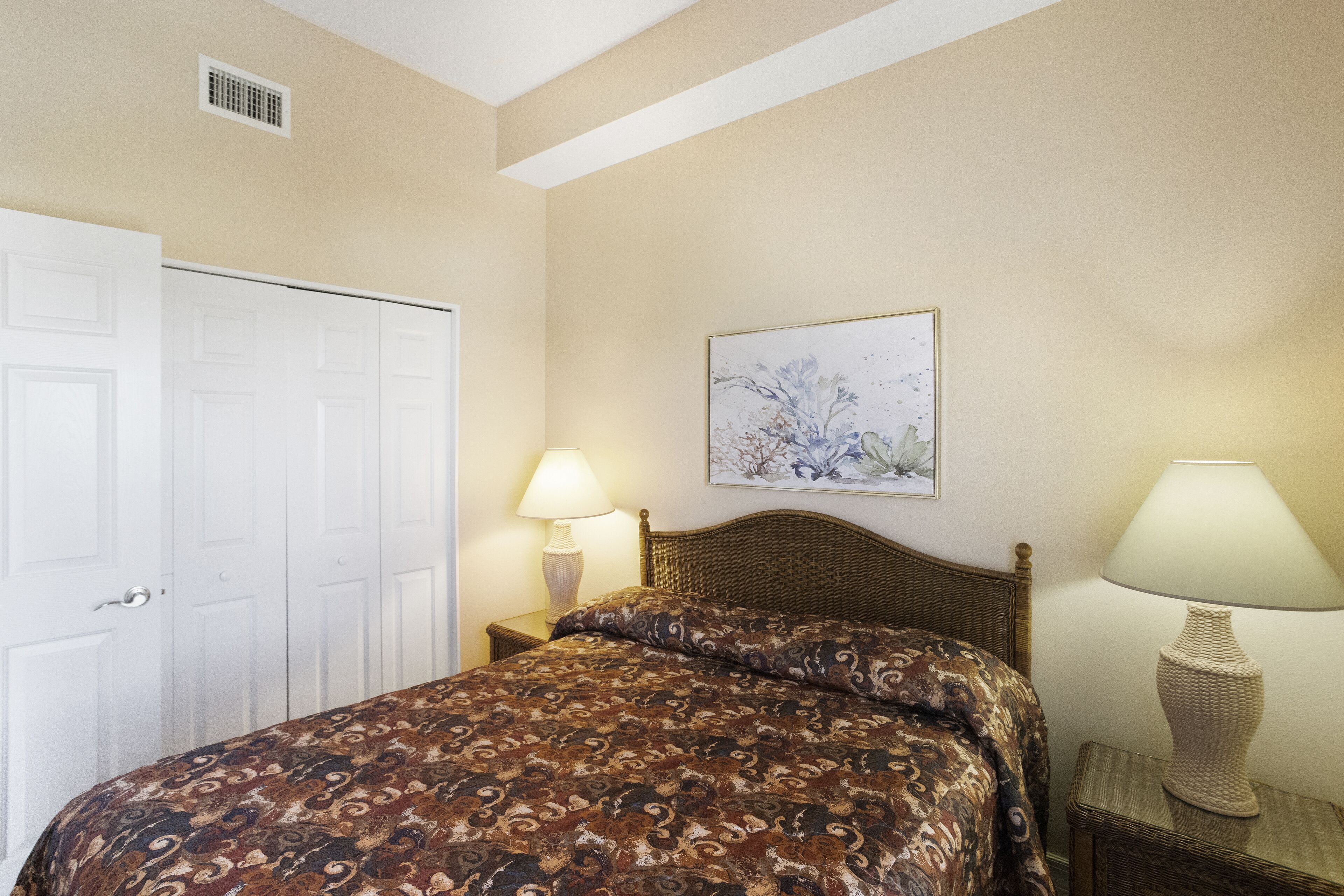 A bedroom with a bed, a nightstand, a lamp, a door, and a wall-mounted picture.