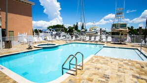 A swimming pool with a lifeguard stand, lounge chairs, and a view of boats in the background.