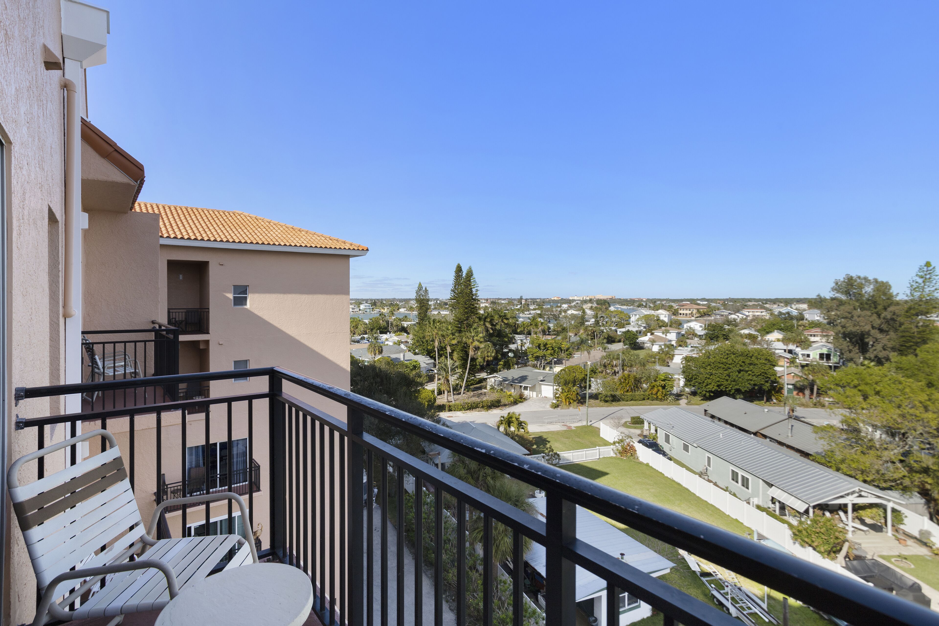A balcony with a table and chairs, overlooking a residential area with houses and trees.